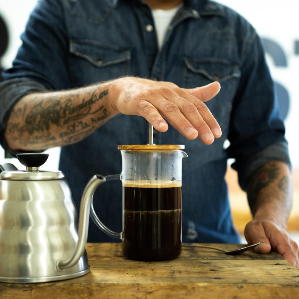 un homme qui presse sur une cafetière à piston (french press)