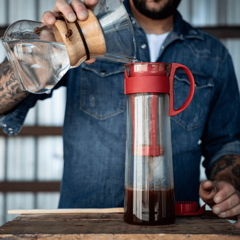 un homme verse de l'eau dans une mizudashi pour faire un café infusé à froid (cold brew)