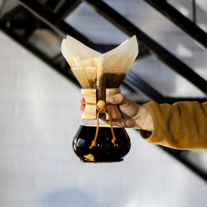 une personne tient un chemex plein de café filtre avec son filtre de papier 